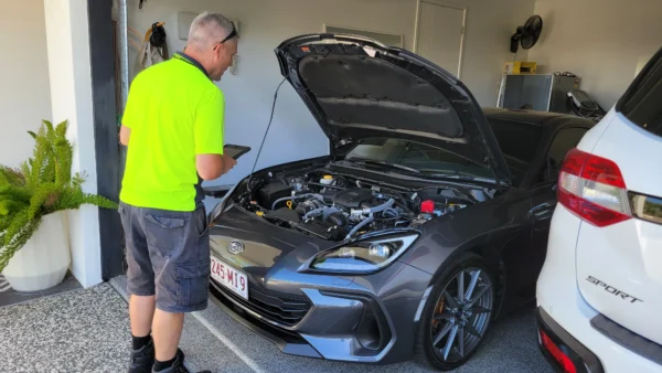 Mechanic using tablet while inspecting Subaru BRZ engine during roadworthy check.