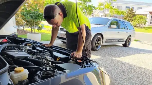 Mobile mechanic checking engine bay for fault diagnosis and service inspection