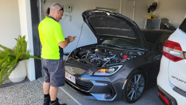 Mechanic inspecting Subaru BRZ with hood open for roadworthy certificate inspection.