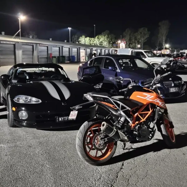 KTM Duke motorbike parked with sports cars at night track inspection event.